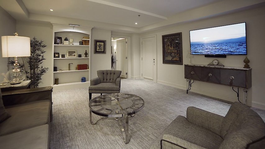 A wide view of a hotel suite's living area with a sofa, chair, coffee table, TV, and bookshelf.