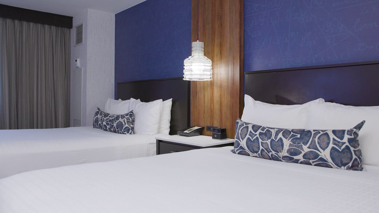 A hotel room with two beds, a blue accent wall, and a pendant light.