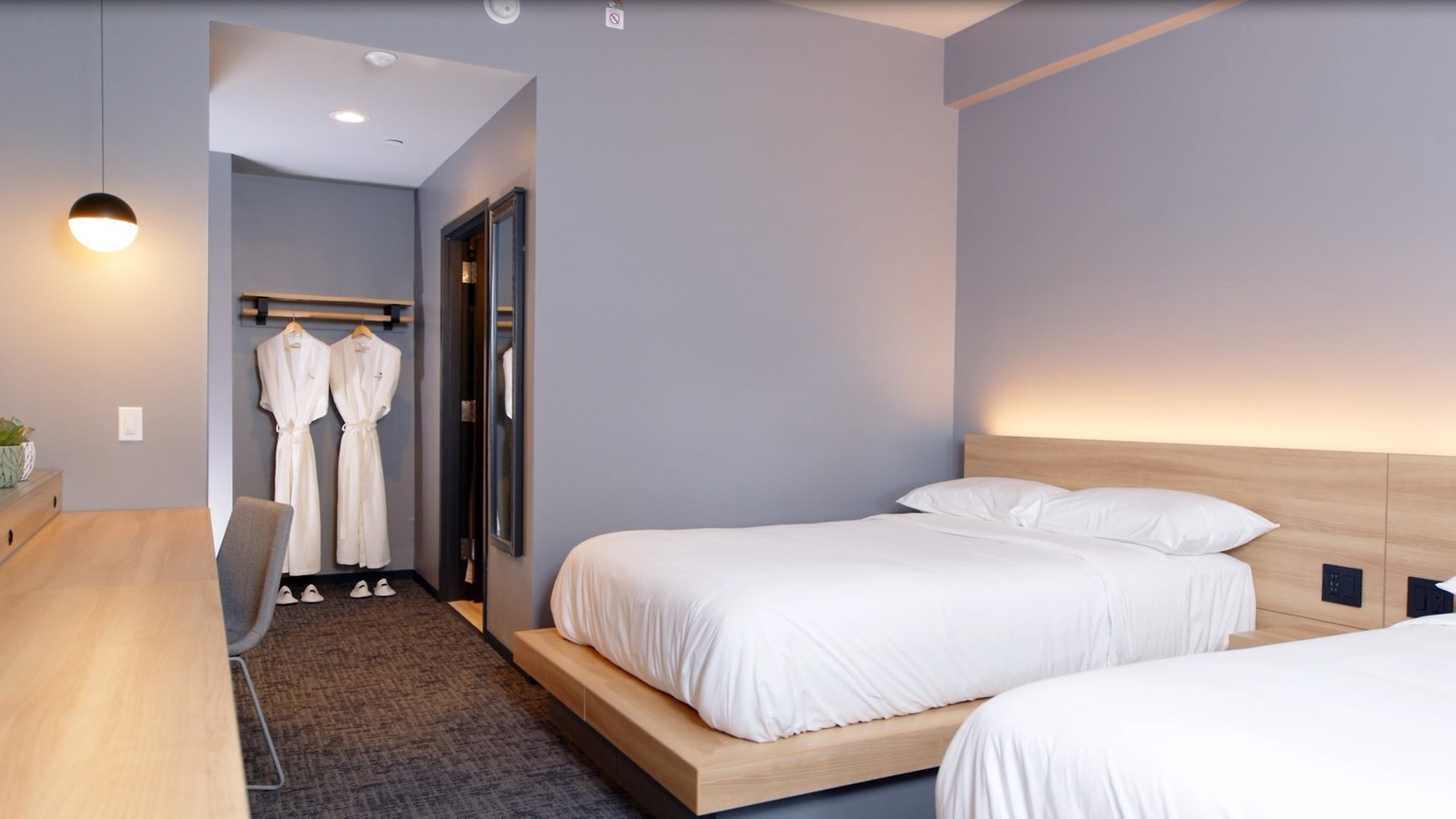 A hotel room with two beds, a desk, and robes hanging on a rack.